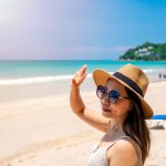Young woman traveler wearing sunglasses covering face by hand to protect UV rays from the sun